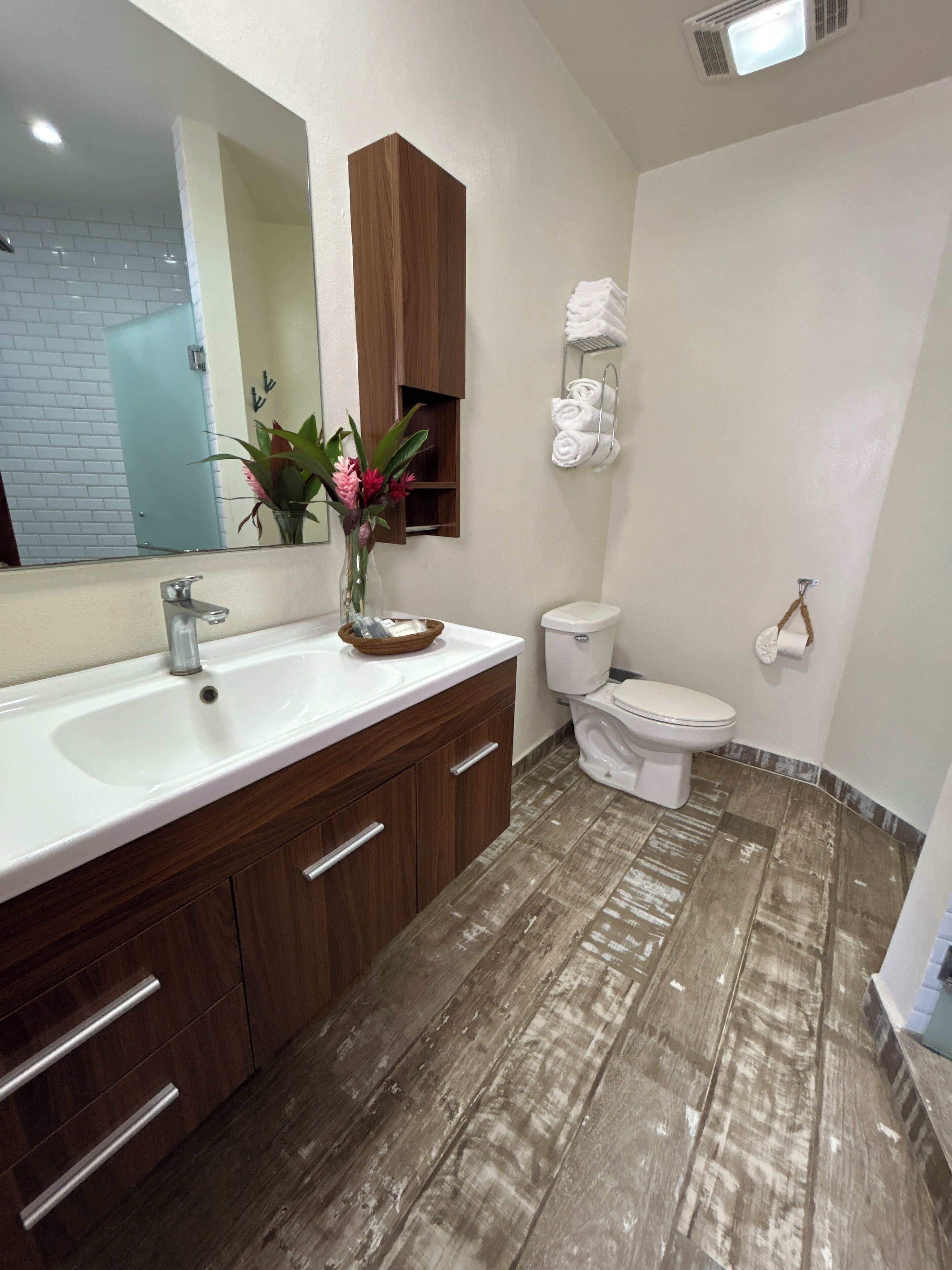 Un baño moderno con lavamanos blanco, tocador de madera y un inodoro.