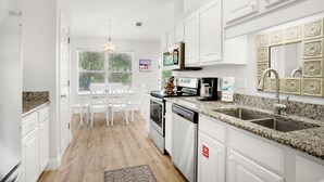 Una cocina moderna con armarios blancos, encimeras de granito y electrodomésticos de acero inoxidable.