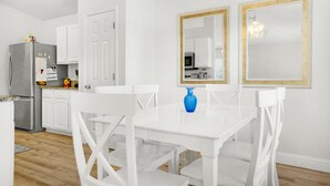 Una cocina moderna con armarios blancos, un refrigerador de acero inoxidable y un comedor con sillas y una mesa blancos.