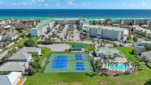 Un complejo turístico con canchas de tenis, piscina y vistas al océano.