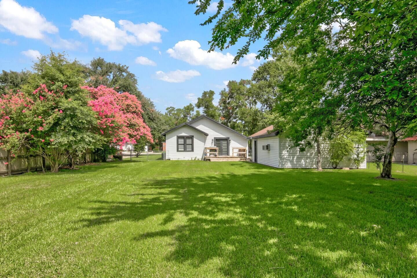 A single-story house with a front porch, surrounded by a well-maintained lawn and trees.