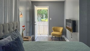 Ein Schlafzimmer mit einem Bett, einem Sessel, einer Tür, die auf einen Balkon führt, und einem an der Wand befestigten Fernseher.