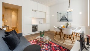 Ett modernt vardagsrum med en grå soffa, ett soffbord i glas och en matplats med vita stolar och ett litet bord.