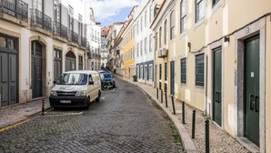 En smal kullerstensgata kantad av höga byggnader, med en parkerad skåpbil och en bil.