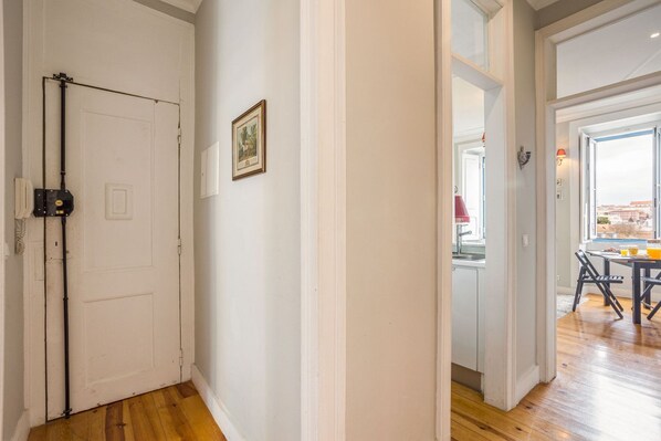 A hallway with a white door, a framed picture on the wall, and a view into a dining area with a table and chairs.