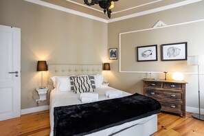 A bedroom with a tufted headboard bed, bedside lamps, a wooden dresser, and framed artwork on the wall.