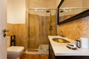 A bathroom with a glass-enclosed shower, a white sink with a gold basin, and marble-patterned walls.