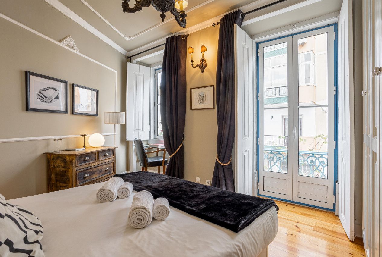Una habitación de hotel con cama, escritorio, silla, cómoda y balcón con cortinas.