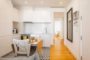 A compact kitchen with white cabinets, a dining table with chairs, and a checkered floor.