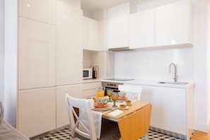 Uma cozinha compacta com armários brancos, micro-ondas, fogão e pia. Há uma mesa de jantar com cadeiras e uma mesa posta para o café da manhã.