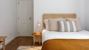 A bedroom with a bed, bedside table, lamp, and a door. - Junqueira · Trendy T.M Apartament by the River (Lisboa)