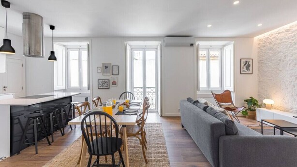 A modern kitchen with a dining area, a sofa, and a stone accent wall. - Junqueira · Trendy T.M Apartament by the River (Lisboa)