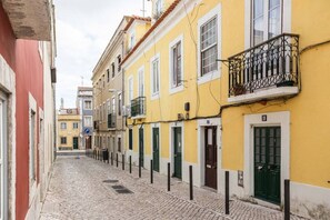 A narrow cobblestone street lined with yellow buildings, each with a balcony and a green door.