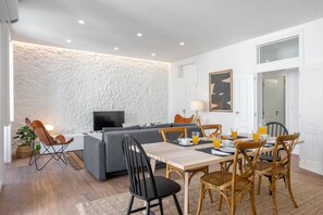 A modern living room with a grey sofa, a dining table set for breakfast, and a TV in the background.