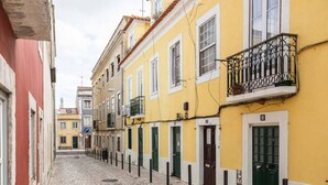 A narrow cobblestone street lined with yellow buildings, each with a balcony and a green door. - Junqueira · Trendy T.M Apartament by the River (Lisboa)