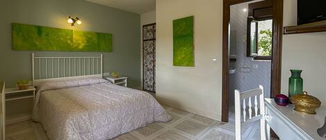 A bedroom with a bed, bedside tables, a desk with a chair, and a television on the wall.