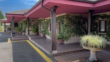 A building with a covered entrance area, potted plants, and a yellow line on the pavement.