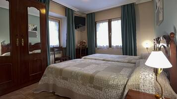 A hotel room with two beds, a wooden wardrobe, a desk with a chair, a TV, and a lamp.