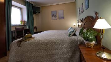 A neatly made bed with a patterned bedspread, a hat on the bed, a bedside lamp, and a potted plant on the nightstand.