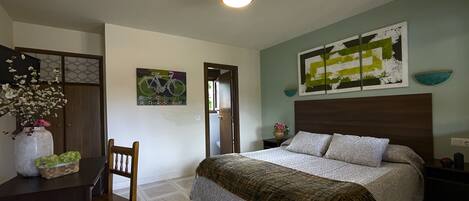 A bedroom with a bed, a desk with a chair, a vase with flowers, and a painting on the wall.