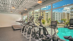 Une salle de sport équipée de tapis de course et dotée d’un espace piscine, de grandes fenêtres et d’une vue sur le paysage urbain.
