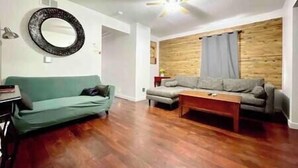 Una sala de estar con un sofá verde, un sofá gris, una pared de madera y un ventilador de techo.