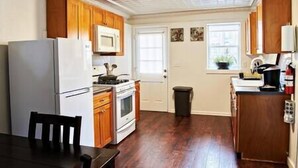 Una cocina con armarios de madera, un refrigerador blanco, una estufa y un microondas. Hay una ventana con una planta en la encimera.