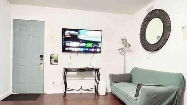 Una sala de estar con un televisor de pantalla plana montado en la pared, un espejo redondo y un sofá verde.