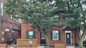 Un edificio de ladrillo de dos plantas con puerta principal, ventanas y un árbol en la fachada.