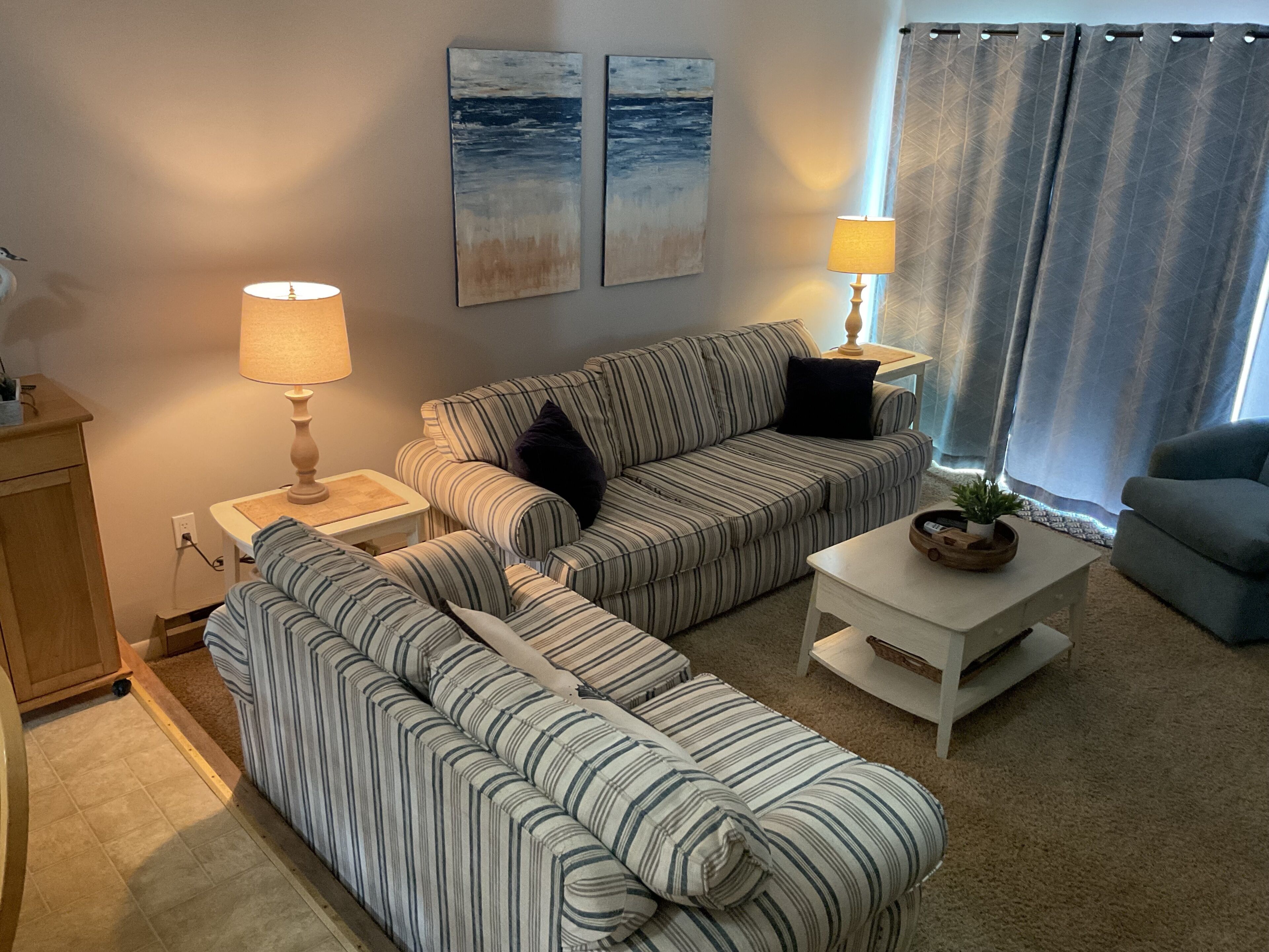 A living room with striped sofas, a coffee table, two lamps, and artwork on the wall.