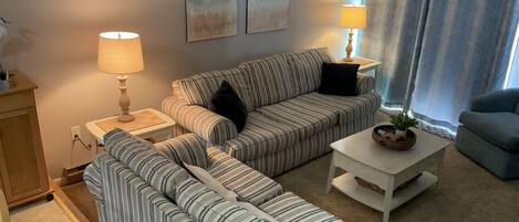 A living room with striped sofas, a coffee table, two lamps, and artwork on the wall.