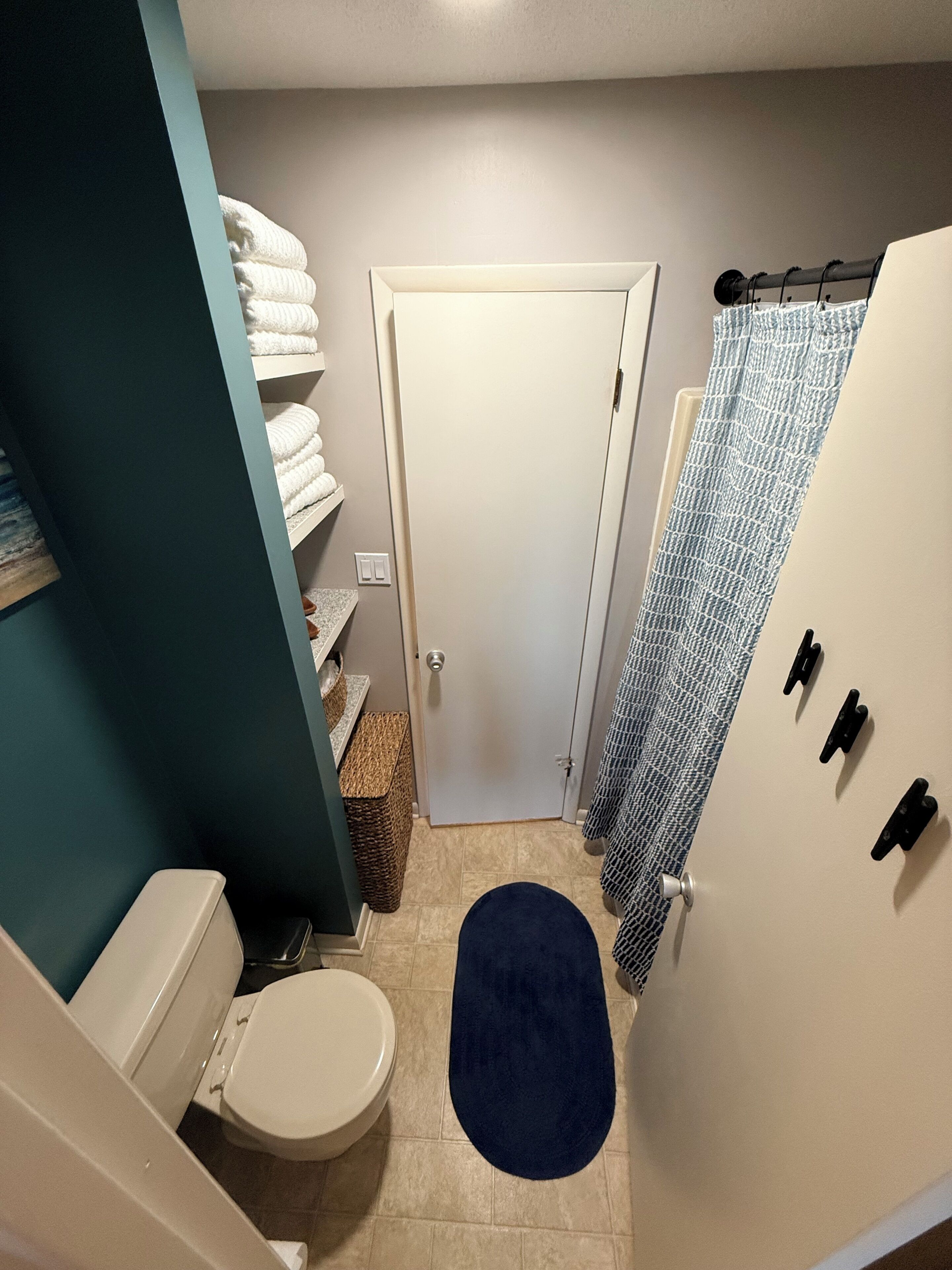 A bathroom with a toilet, a sink, a towel rack, a shower curtain, and a door.