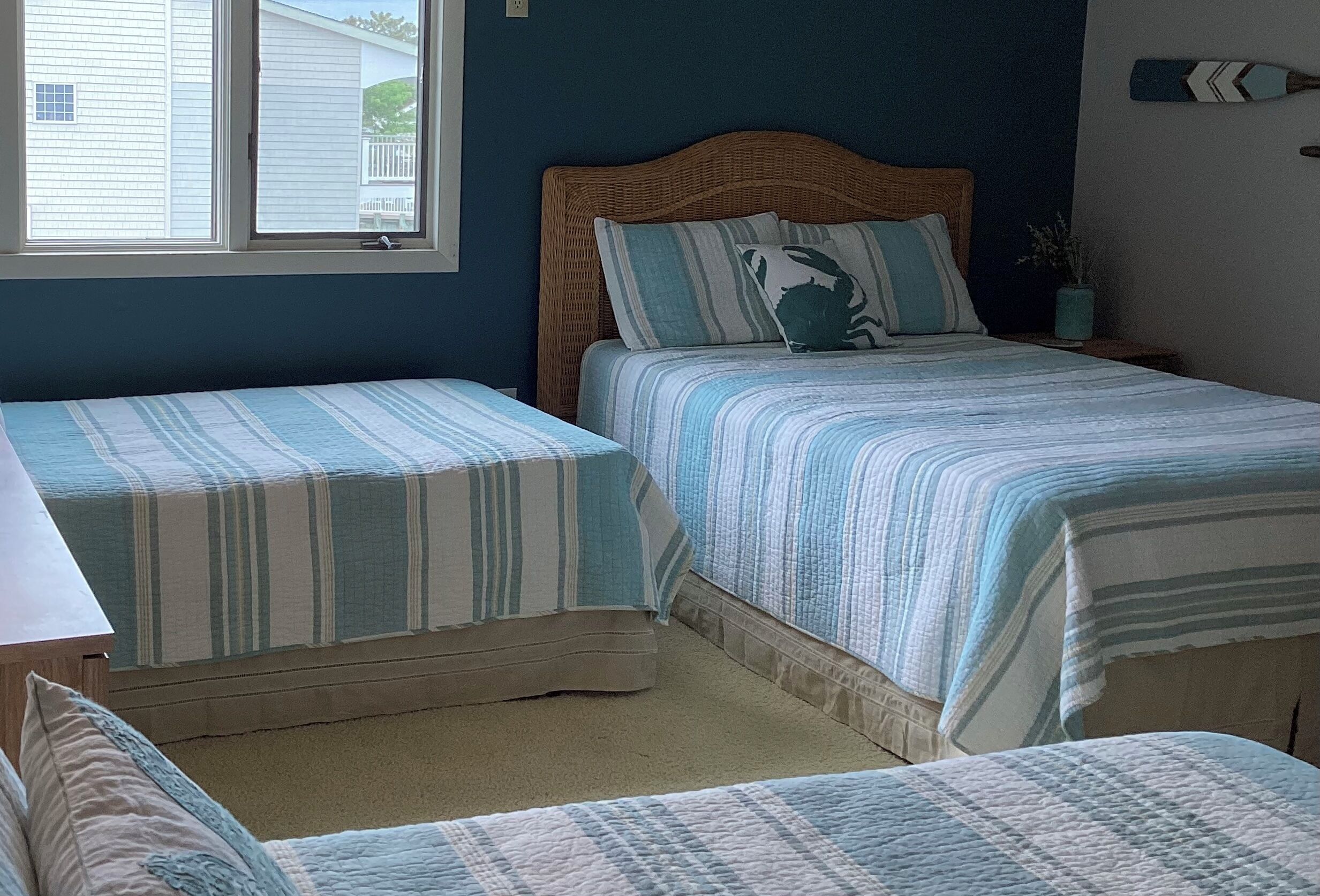 A bedroom with two beds, a window, a wooden headboard, and a small potted plant.