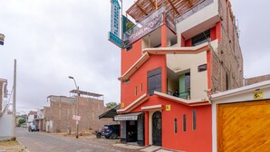 A multi-story building with a red facade, a visible garage door, and a street in front. - Hospedaje Muñoz (Ica)