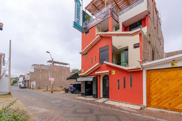 A multi-story building with a red facade, a visible garage door, and a street in front. - Hospedaje Muñoz (Ica)