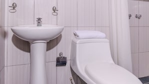 A bathroom with a white pedestal sink, a toilet, and a towel on the toilet seat. - Hospedaje Muñoz (Ica)