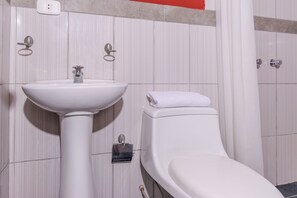 A bathroom with a white pedestal sink, a toilet, and a towel on the toilet seat. - Hospedaje Muñoz (Ica)