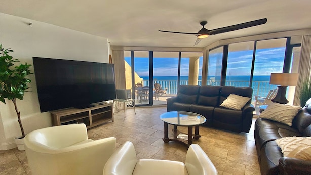 A spacious living room with a large flat-screen TV, comfortable seating, a ceiling fan, and a balcony with a view of the ocean. - Luxury Direct Ocean Front- 3 bed-3 bath with Large Balcony<br>One Ocean Place (Murrells Inlet)