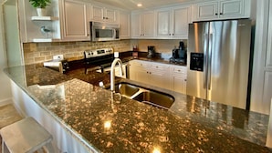 A modern kitchen with white cabinets, a stainless steel refrigerator, granite countertops, and a built-in microwave. - Luxury Direct Ocean Front- 3 bed-3 bath with Large Balcony<br>One Ocean Place (Murrells Inlet)