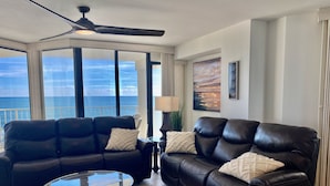 A living room with two black leather sofas, a glass coffee table, and a ceiling fan. Large windows offer a view of the ocean. - Luxury Direct Ocean Front- 3 bed-3 bath with Large Balcony<br>One Ocean Place (Murrells Inlet)