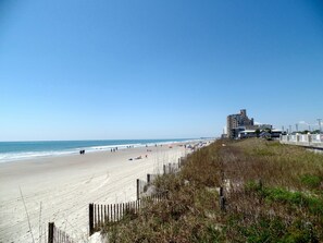 Une plage avec une clôture en bois, une jetée et des bâtiments en arrière-plan.