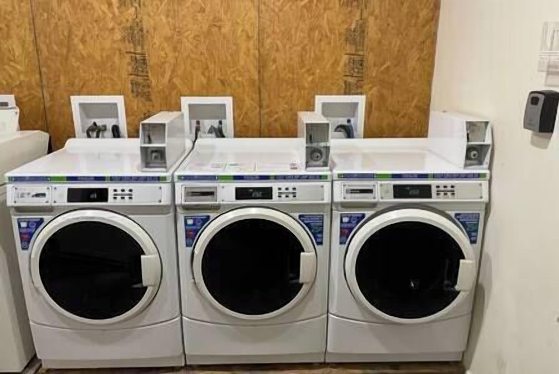 A row of three front-loading washing machines in a commercial setting.