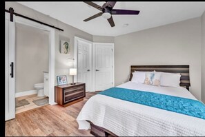 Relax in this serene bedroom with a large bed, ceiling fan, and a nightstand with a lamp and picture frame.