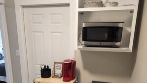 A compact kitchenette with a microwave, a mini-fridge, a coffee maker, and a small cart with cups and a trash bin. - Large newly renovated family home. Sleeps 15. Walking distance to everything. (Oak Island)