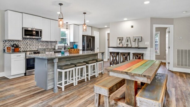 A modern kitchen with white cabinets, a large island with bar stools, a microwave, and a refrigerator. - Large newly renovated family home. Sleeps 15. Walking distance to everything. (Oak Island)