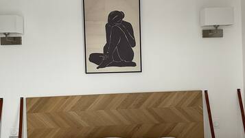 Ein Hotelzimmer mit einem Holzboden-Kopfteil, einem Bett mit weißblauen Kissen und einem gerahmten Kunstwerk einer sitzenden Person an der Wand.