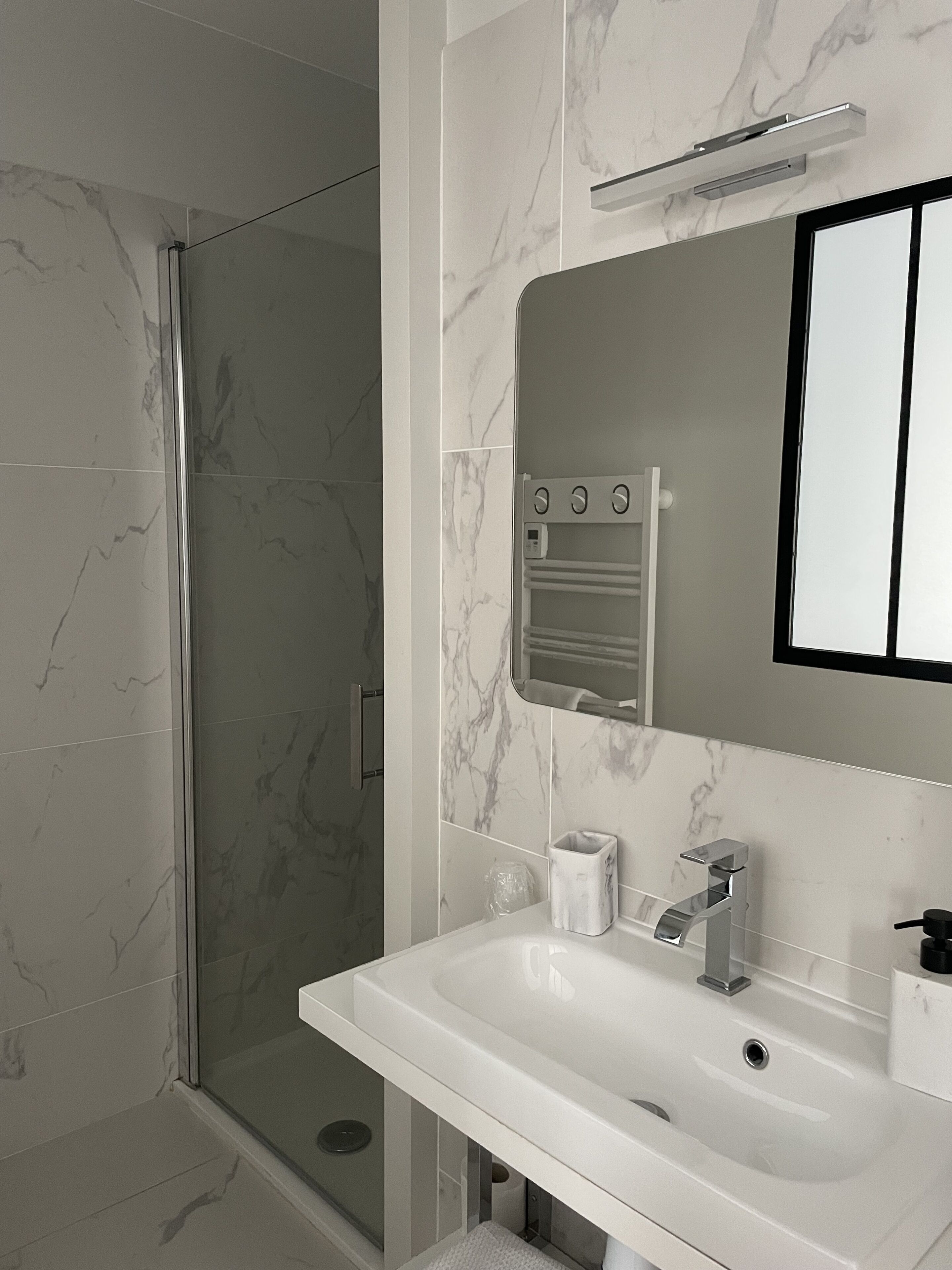 Un baño moderno con cabina de ducha de vidrio, un lavabo blanco y una salpicadura de mármol.