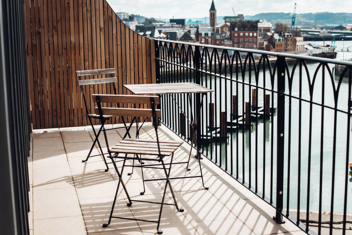 A balcony with a wooden wall, a metal railing, and a view of a river with buildings in the background.