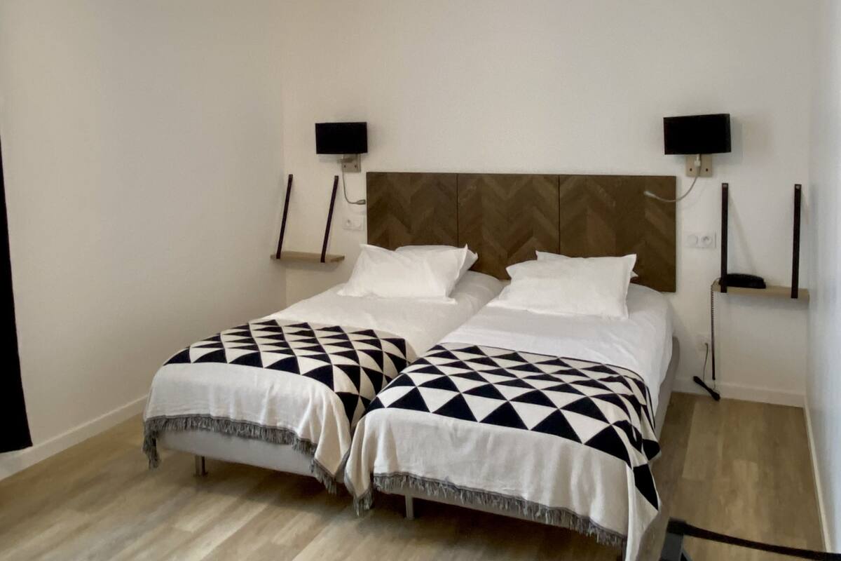 A bedroom with two beds, a wooden headboard, bedside lamps, and a hanging light fixture.