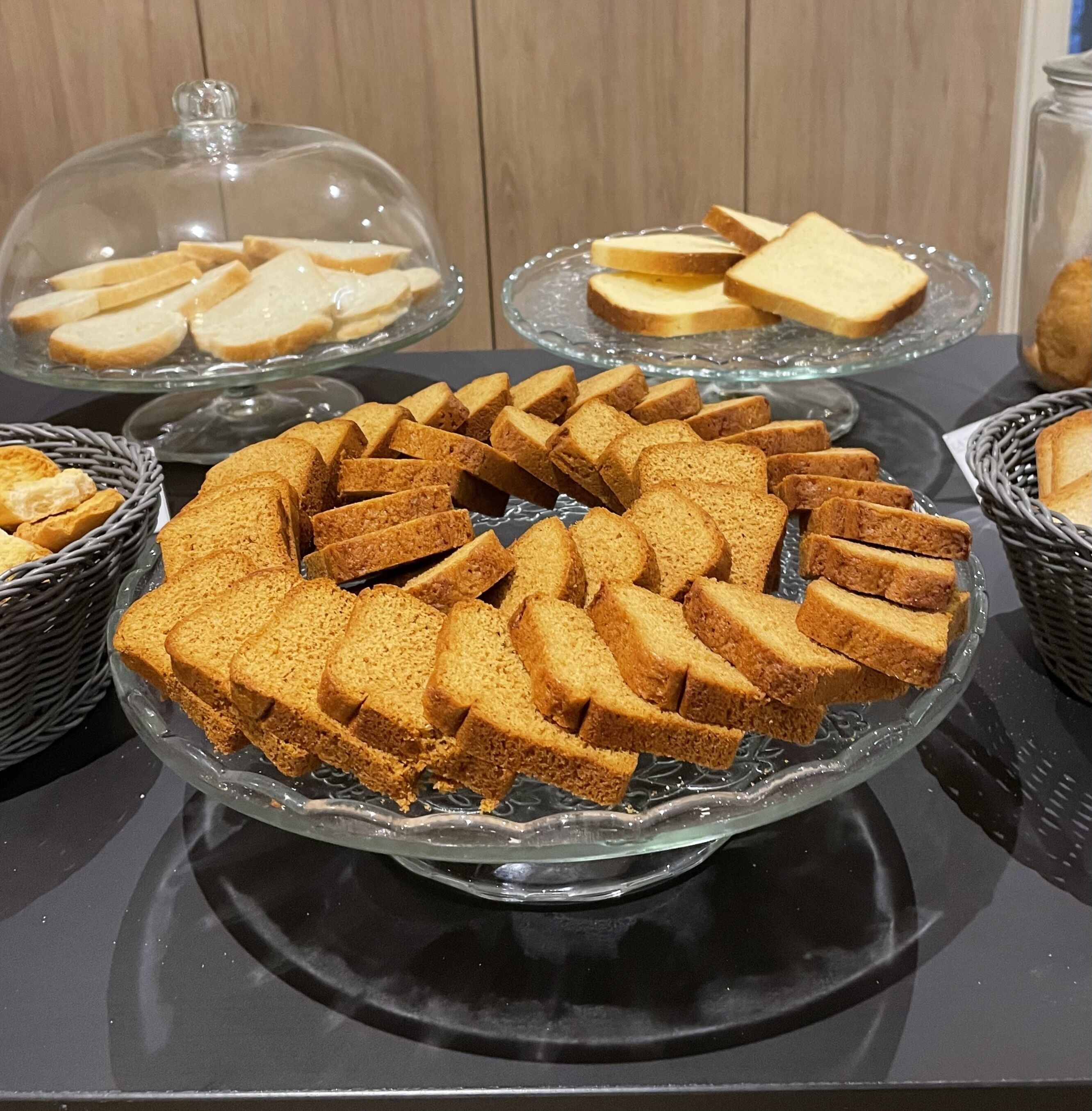 A buffet table with various bread items, including a large bread cake and slices of bread on glass stands.
